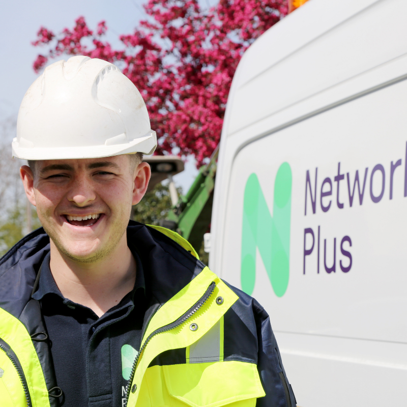 Employee in PPE smiling, standing next to Network Plus Van