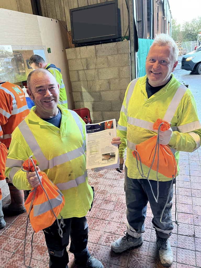 Two Network Plus colleagues smiling at camera, wearing PPE and holding a a bag. 